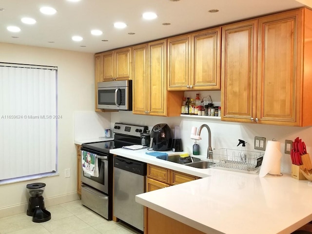 kitchen with appliances with stainless steel finishes, light tile patterned floors, sink, and kitchen peninsula