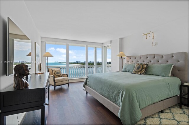 bedroom featuring dark hardwood / wood-style floors, expansive windows, and a water view