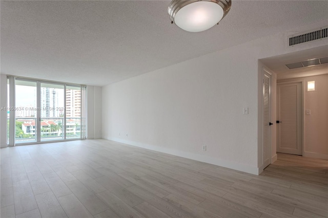 unfurnished room featuring a textured ceiling, light wood-type flooring, and a wall of windows