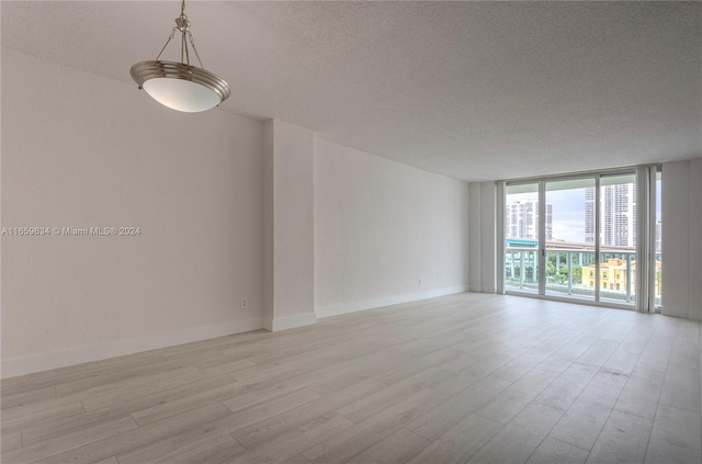 empty room with light wood-type flooring, a textured ceiling, and a wall of windows