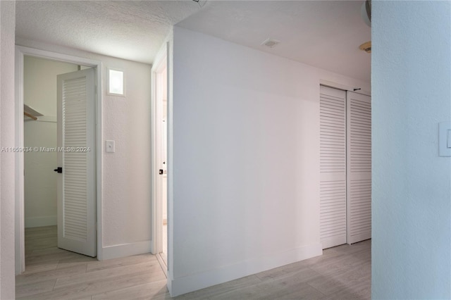 corridor featuring a textured ceiling and light hardwood / wood-style floors