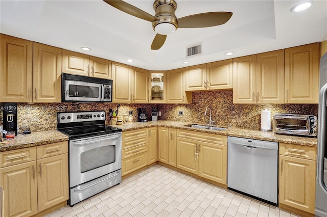 kitchen with sink, light stone counters, ceiling fan, stainless steel appliances, and decorative backsplash