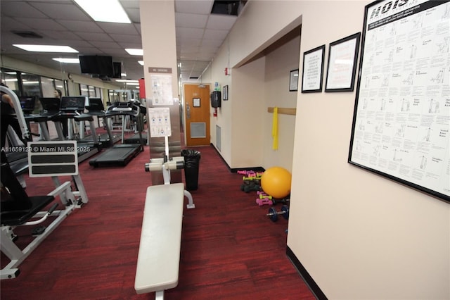 exercise room featuring a paneled ceiling and dark colored carpet