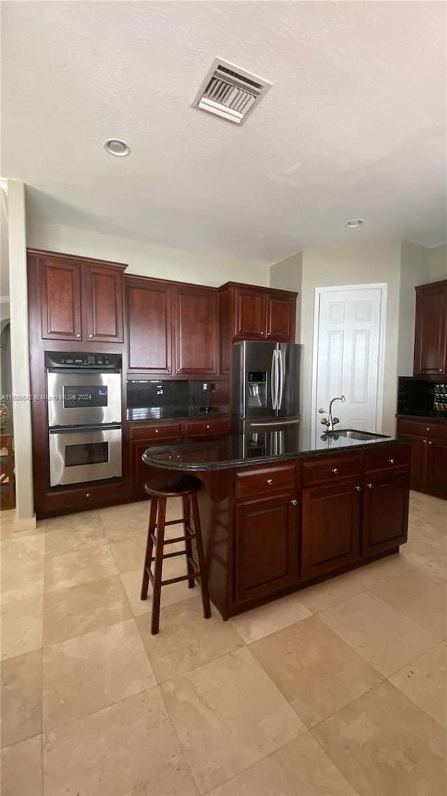 kitchen featuring light tile patterned floors, a kitchen breakfast bar, sink, an island with sink, and appliances with stainless steel finishes