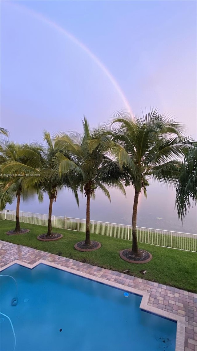 pool at dusk featuring a yard and a water view