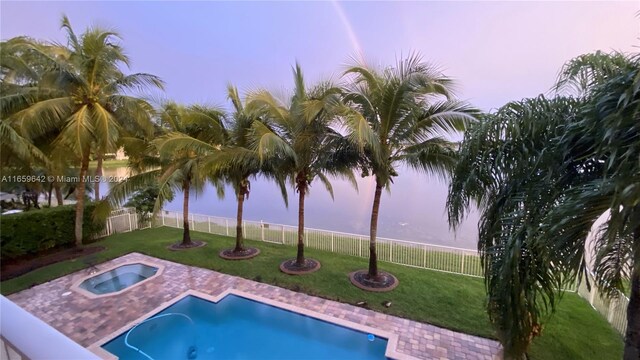 pool at dusk featuring a water view, a yard, and a patio