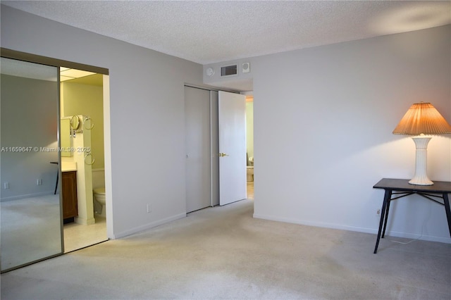 unfurnished bedroom with carpet floors, visible vents, connected bathroom, and a textured ceiling