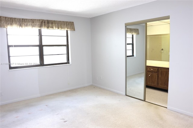 unfurnished bedroom featuring a textured ceiling, connected bathroom, a closet, and light carpet