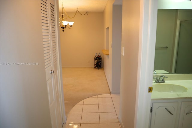 hall with carpet floors, an inviting chandelier, a sink, tile patterned flooring, and baseboards