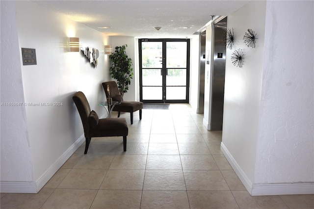 hall featuring light tile patterned floors, elevator, and a textured ceiling