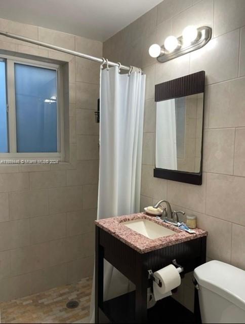 bathroom with vanity, toilet, tile walls, and walk in shower