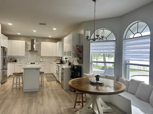 kitchen with white cabinetry, a center island, wall chimney exhaust hood, stainless steel fridge with ice dispenser, and pendant lighting