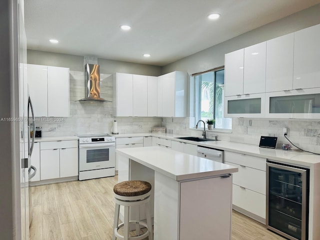 kitchen with sink, wall chimney exhaust hood, stainless steel appliances, beverage cooler, and white cabinets