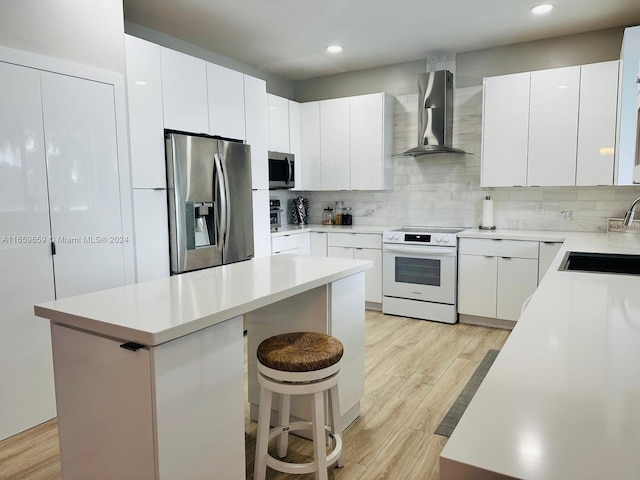 kitchen featuring appliances with stainless steel finishes, a kitchen island, white cabinetry, and wall chimney exhaust hood