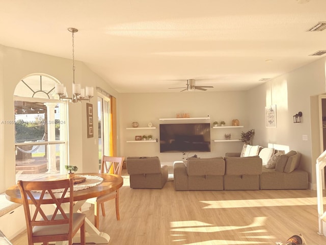 living room featuring lofted ceiling, ceiling fan with notable chandelier, and light wood-type flooring