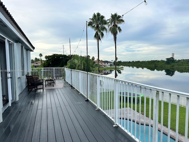 wooden deck featuring a lawn, a water view, and a fenced in pool