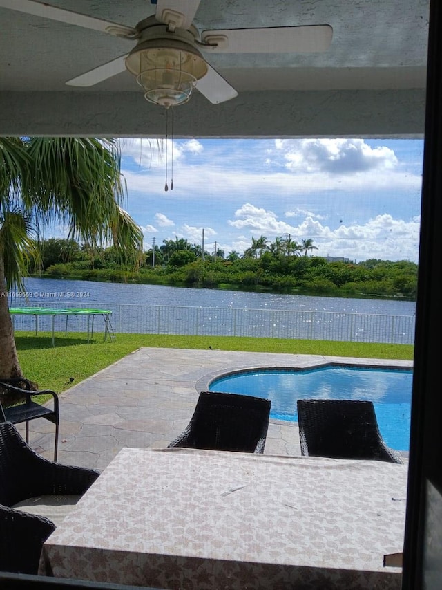 view of pool with a trampoline, a water view, ceiling fan, a yard, and a patio area