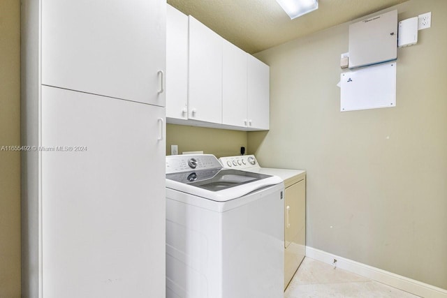 laundry room featuring a textured ceiling, cabinets, light tile patterned floors, and washing machine and dryer