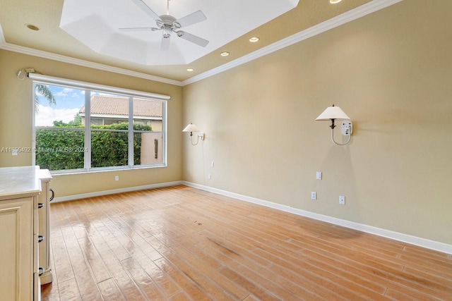 empty room featuring a raised ceiling, ceiling fan, ornamental molding, and light wood-type flooring