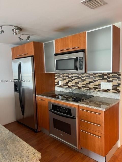 kitchen featuring light stone countertops, decorative backsplash, stainless steel appliances, and dark hardwood / wood-style floors