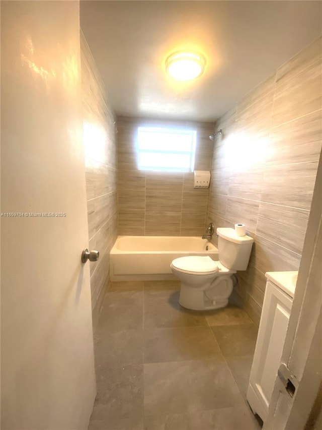 full bathroom with tile patterned floors, toilet, tiled shower / bath, tile walls, and vanity