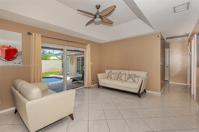 living room with a tray ceiling, a textured ceiling, light tile patterned flooring, and ceiling fan