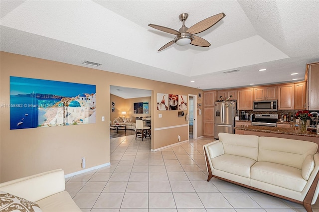 tiled living room with a textured ceiling, ceiling fan, and a tray ceiling