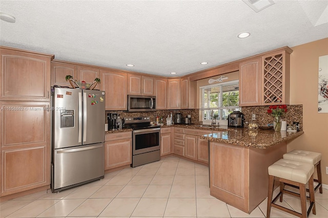 kitchen with appliances with stainless steel finishes, sink, kitchen peninsula, dark stone counters, and a breakfast bar area