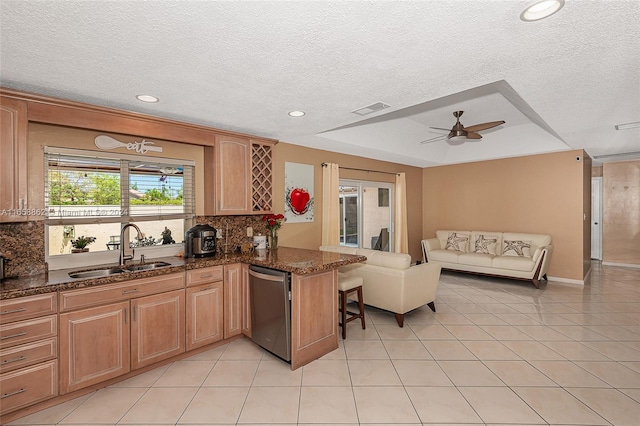 kitchen with a textured ceiling, sink, dark stone counters, ceiling fan, and stainless steel dishwasher