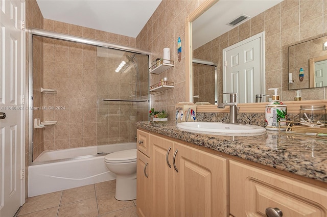 full bathroom featuring toilet, tile patterned flooring, vanity, bath / shower combo with glass door, and tile walls