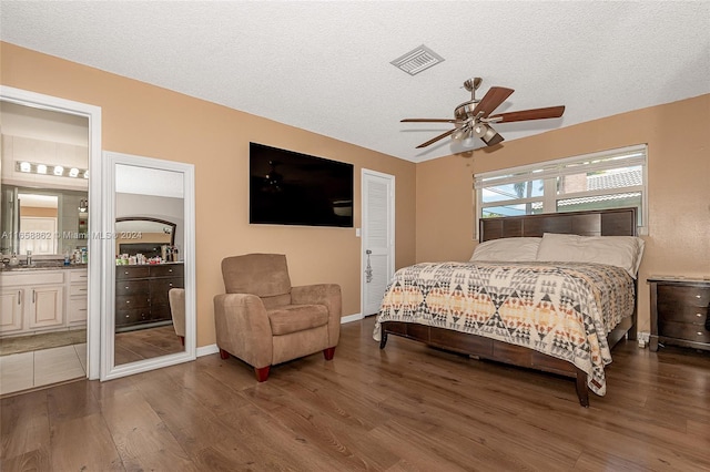 bedroom featuring dark wood-type flooring, ceiling fan, ensuite bathroom, and a textured ceiling