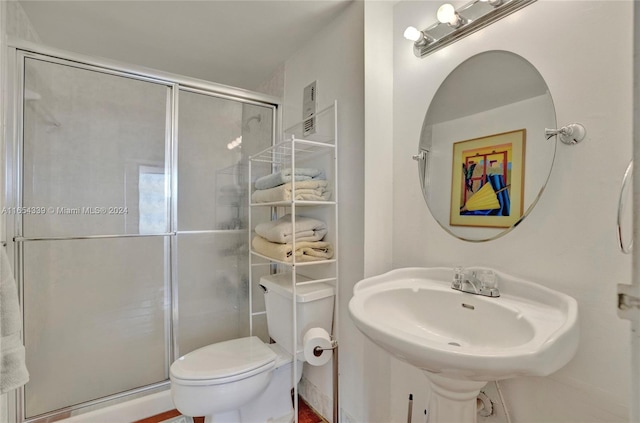 bathroom featuring toilet, sink, and a shower with door