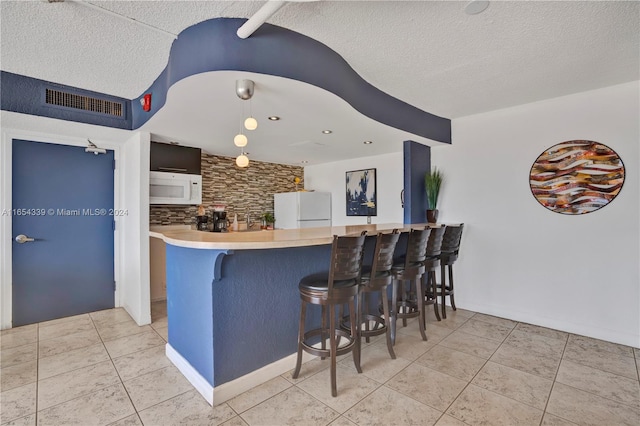 kitchen featuring white appliances, backsplash, kitchen peninsula, hanging light fixtures, and a breakfast bar