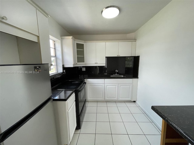 kitchen with fridge, black range with electric cooktop, light tile patterned floors, white cabinets, and tasteful backsplash