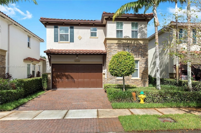 mediterranean / spanish home featuring decorative driveway, a tile roof, stucco siding, a garage, and stone siding