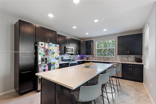 kitchen with stainless steel appliances, backsplash, a sink, a kitchen island, and a kitchen breakfast bar