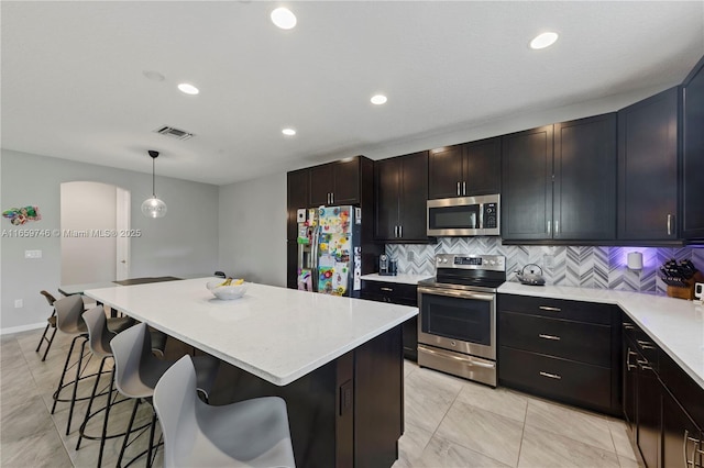 kitchen featuring a breakfast bar area, stainless steel appliances, visible vents, light countertops, and a center island