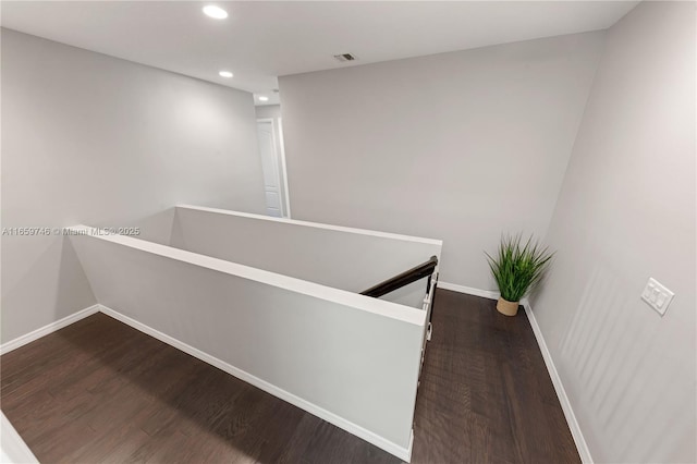 hallway with baseboards, visible vents, dark wood finished floors, and an upstairs landing