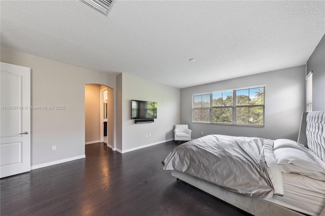 bedroom featuring arched walkways, a textured ceiling, wood finished floors, visible vents, and baseboards