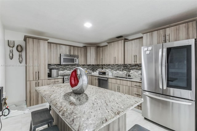 kitchen featuring light stone countertops, backsplash, a center island, stainless steel appliances, and sink