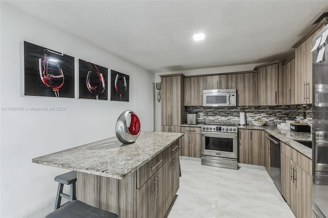 kitchen featuring backsplash, a breakfast bar, stainless steel appliances, a center island, and light stone counters