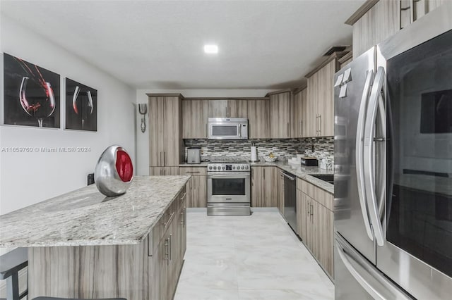 kitchen with stainless steel appliances, a kitchen breakfast bar, a center island, light stone countertops, and decorative backsplash