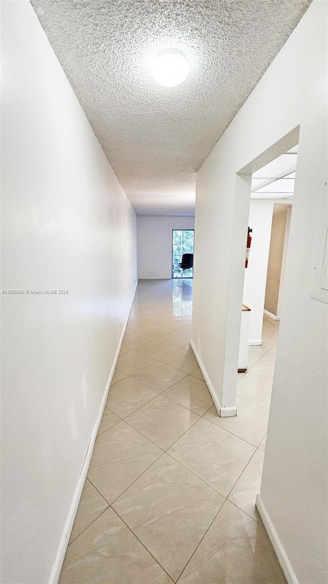 hall with a textured ceiling and light tile patterned floors