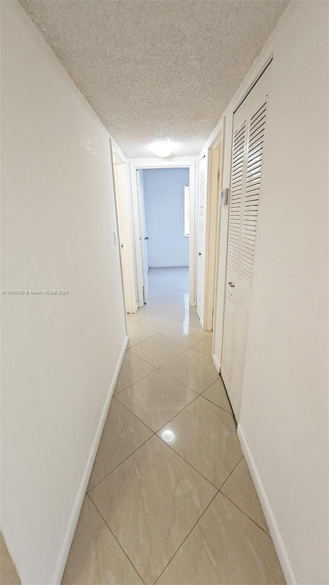 corridor featuring a textured ceiling and light tile patterned flooring