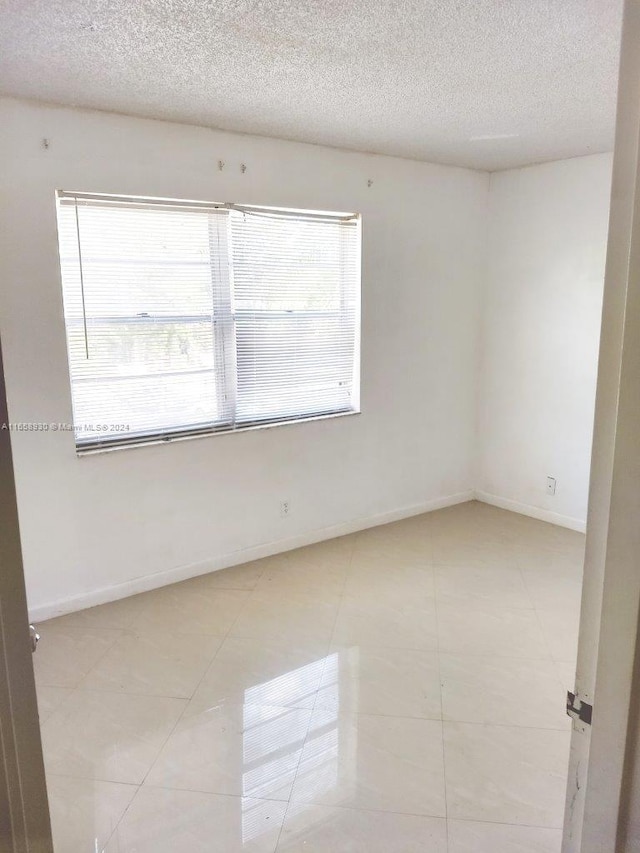 empty room featuring a wealth of natural light, light tile patterned flooring, and a textured ceiling