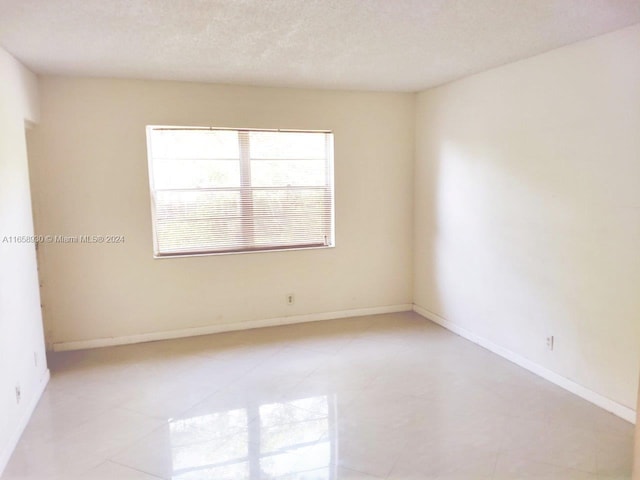 spare room with a textured ceiling and light tile patterned flooring