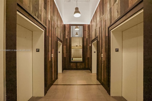 hall featuring wood walls, light tile patterned floors, elevator, and a towering ceiling