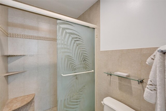 bathroom with tile walls, toilet, and a shower with door