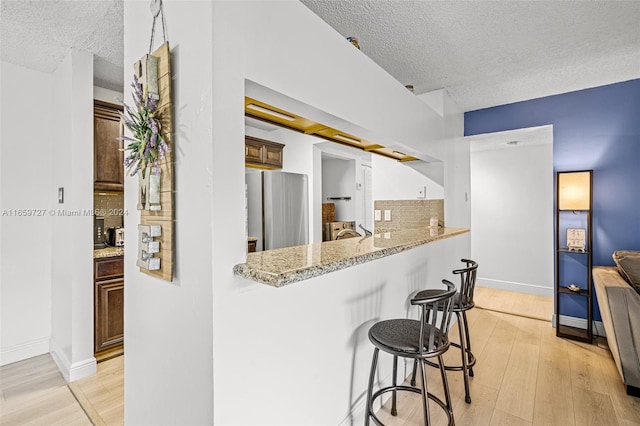 kitchen with stainless steel fridge, a kitchen bar, light hardwood / wood-style floors, and a textured ceiling