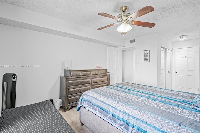 bedroom with a textured ceiling, ceiling fan, and light hardwood / wood-style floors